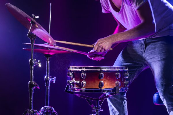 A drummer plays drums on a blue background. Beautiful special effects of light and smoke. The process of playing a musical instrument. A drummer plays drums on a blue background. Beautiful special effects of light and smoke. The process of playing a musical instrument. The concept of music. Close-up photo.